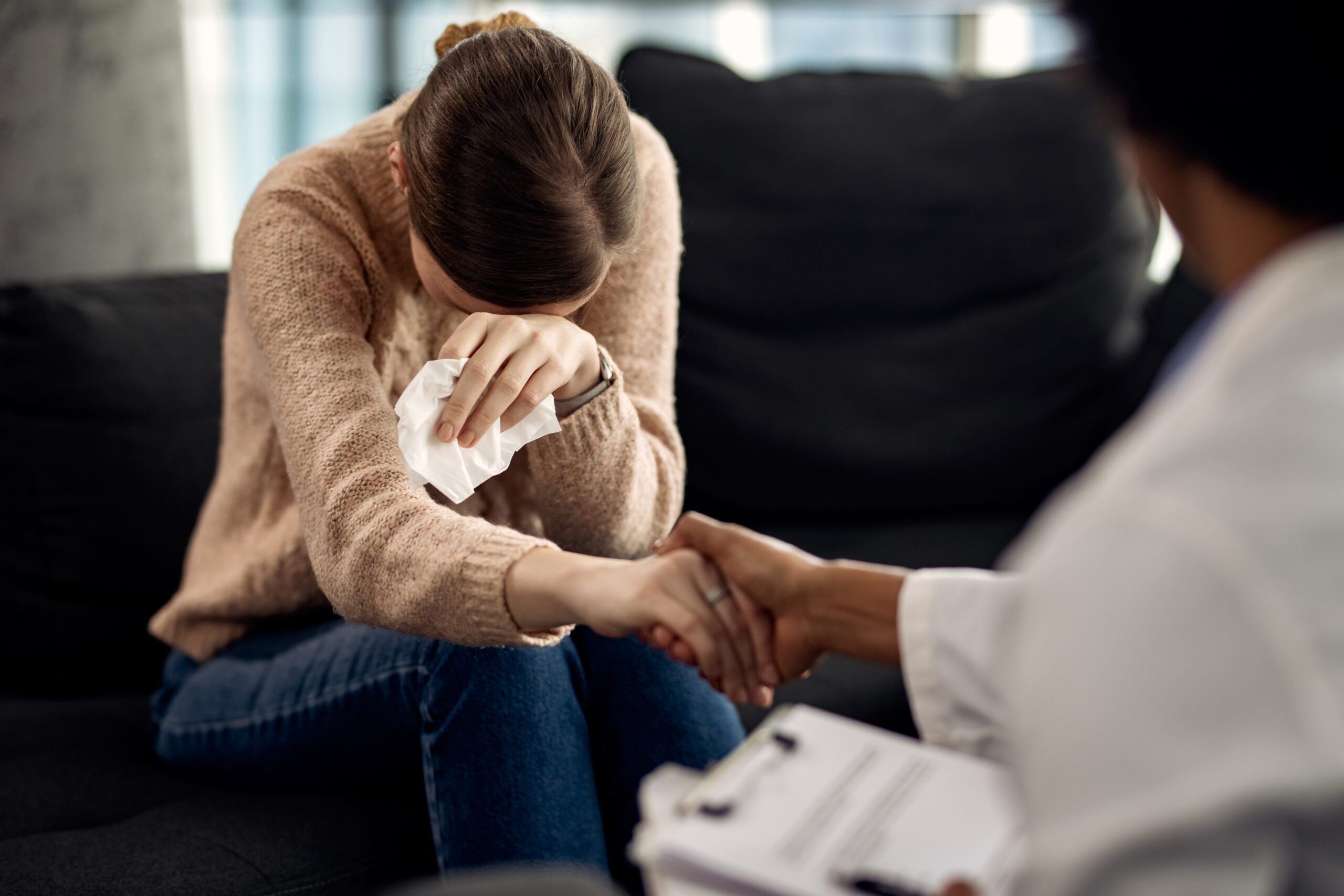 Sad woman crying while holding hands with her psychotherapist at doctor's office.